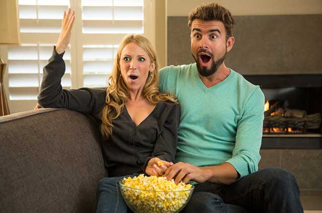 Couple on couch watching Netflix and sharing a bowl of popcorn.